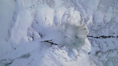 Aerial-top-view-over-Skogafoss-waterfall,-in-a-winter-landscape-covered-in-snow,-in-Iceland,-at-sunset