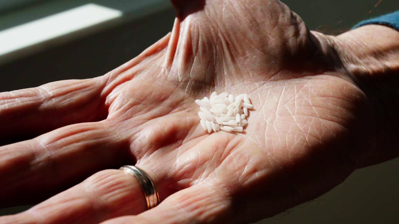 elderly man's hand holding the last rice kernels he has in his home