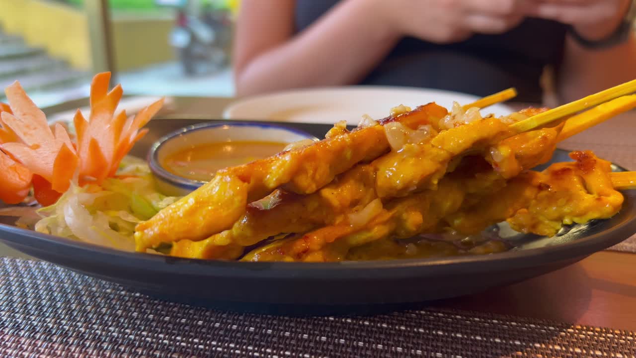 Brochettes de poulet satay thaïlandaises traditionnelles avec sauce aux arachides et carottes en restaurant, mets asiatique savoureux, vidéo 4K