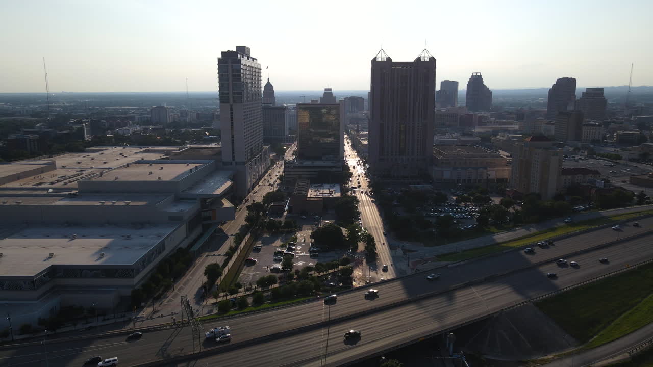 A stunning 4K aerial shot of downtown San Antonio captures the city skyline with the sun setting behind the buildings and a quiet highway in the foreground, highlighting the tranquil urban landscape.