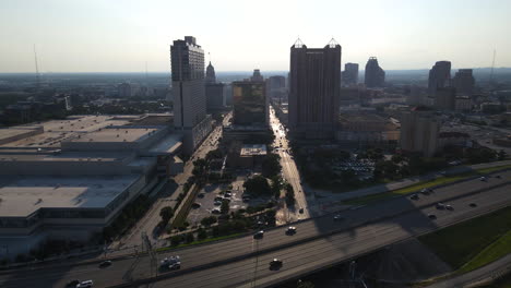 a stunning 4k aerial shot of downtown san antonio captures the city skyline with the sun setting behind the buildings and a quiet highway in the foreground, highlighting the tranquil urban landscape.