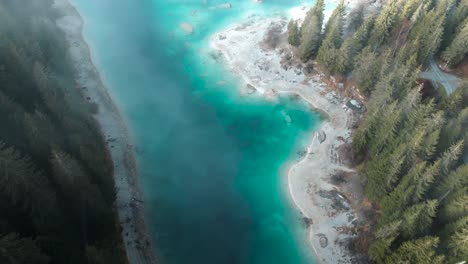 drone flying through clouds showing a pristine blue water lake caumasee with forests around in switzerland