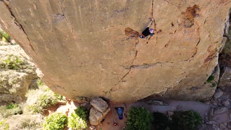 Man-rock-climbing-aerial-view-of-sportsman-rapelling-mountain-in-La-Panocha,-el-Valle-Murcia,-Spain-woman-rapel-down-a-mountain-climbing-a-big-rock