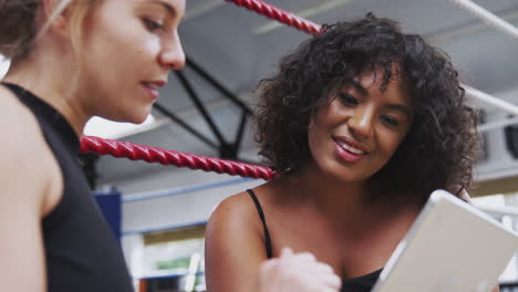 female personal trainer with female boxer in gym checking performance using digital tablet