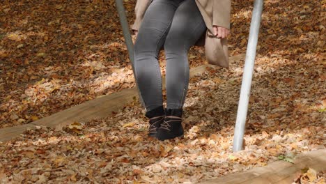 low angle shot of woman with boots sitting on swing and playing with falling leaves in ocotber - slow motion