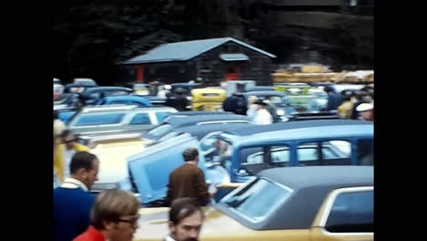 group of people gathered around a parking lot at an old car show in the 1970s, usa. circa usa - 1970s: a group of people, enthusiasts and visitors, stand around a parking lot during an old car show in the 1970s in the usa.