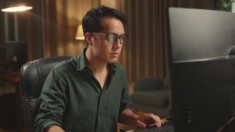 asian male works his personal computer. he works at night