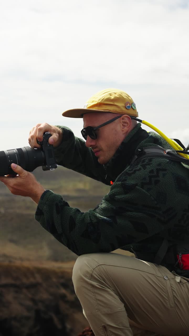 Mandlig fotograf sidder på hug og tager billeder i et klippefyldt bjerglandskab