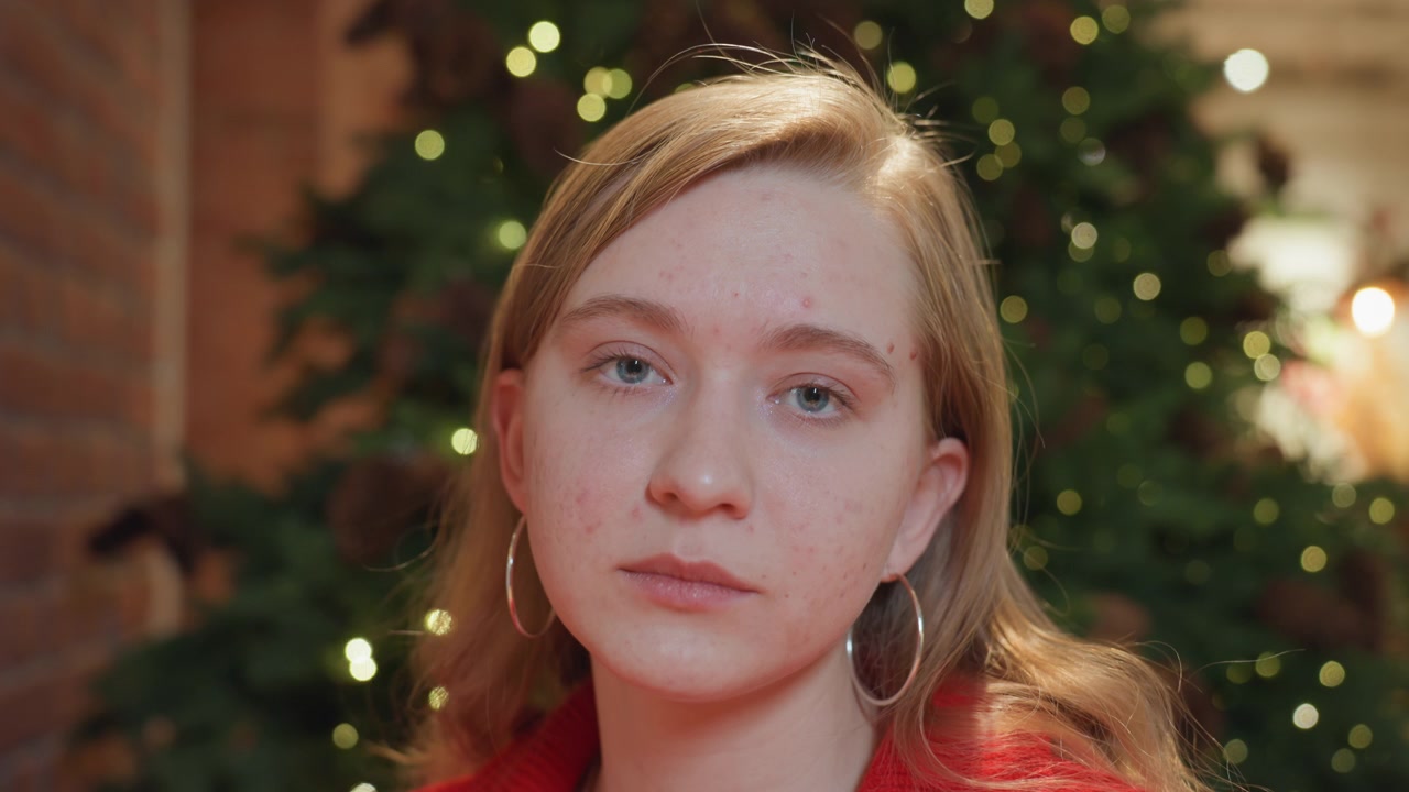 Giovane donna pensierosa che guarda la fotocamera davanti a un albero di Natale