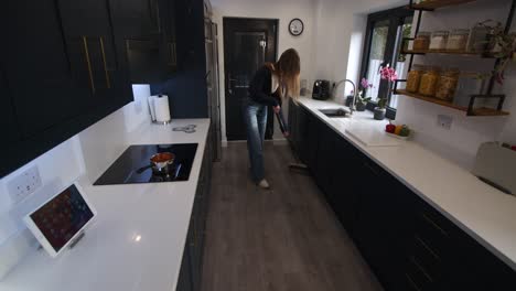wide-shot-of-a-model-sweeping-a-wood-floor-in-a-modern-kitchen