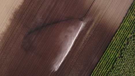 Draufsicht-Auf-Den-Bewässerungssprinkler,-Der-Wasser-Auf-Trockenem-Boden-Eines-Landwirtschaftlichen-Betriebes-Verteilt