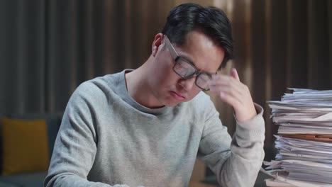 close up of tired asian man shaking his head while working hard with documents at home