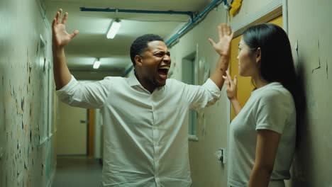 toxic relationship dynamics unfolding, showing partner experiencing terror while aggressive man shouting menacingly in dark, narrow hallway, revealing intense domestic conflict