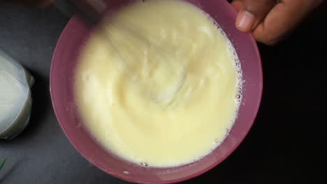 beating and mixing egg with buttermilk in a purple coloured bowl by whisk with hand