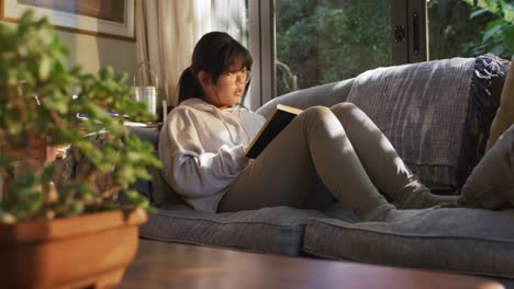 Asian-girl-lying-on-couch-and-reading-book