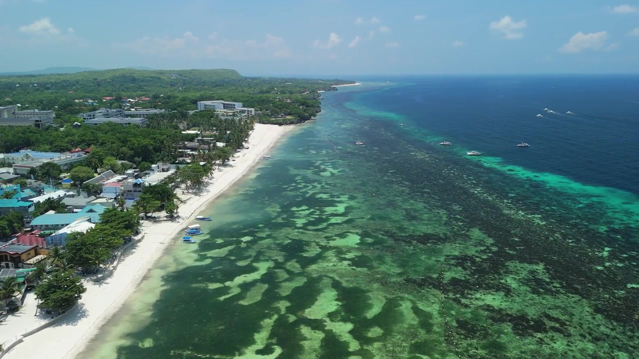 Il drone orbita a sinistra sopra Alona Beach, rivelando sabbia bianca, acque basse della barriera corallina, barche, resort e la costa di Panglao a Bohol