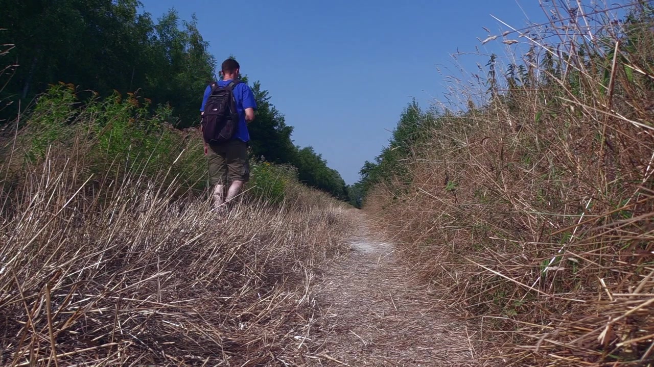 Uomo che cammina su una strada sterrata e si dirige verso il bosco, mentre beve e getta via la sua bottiglia vuota