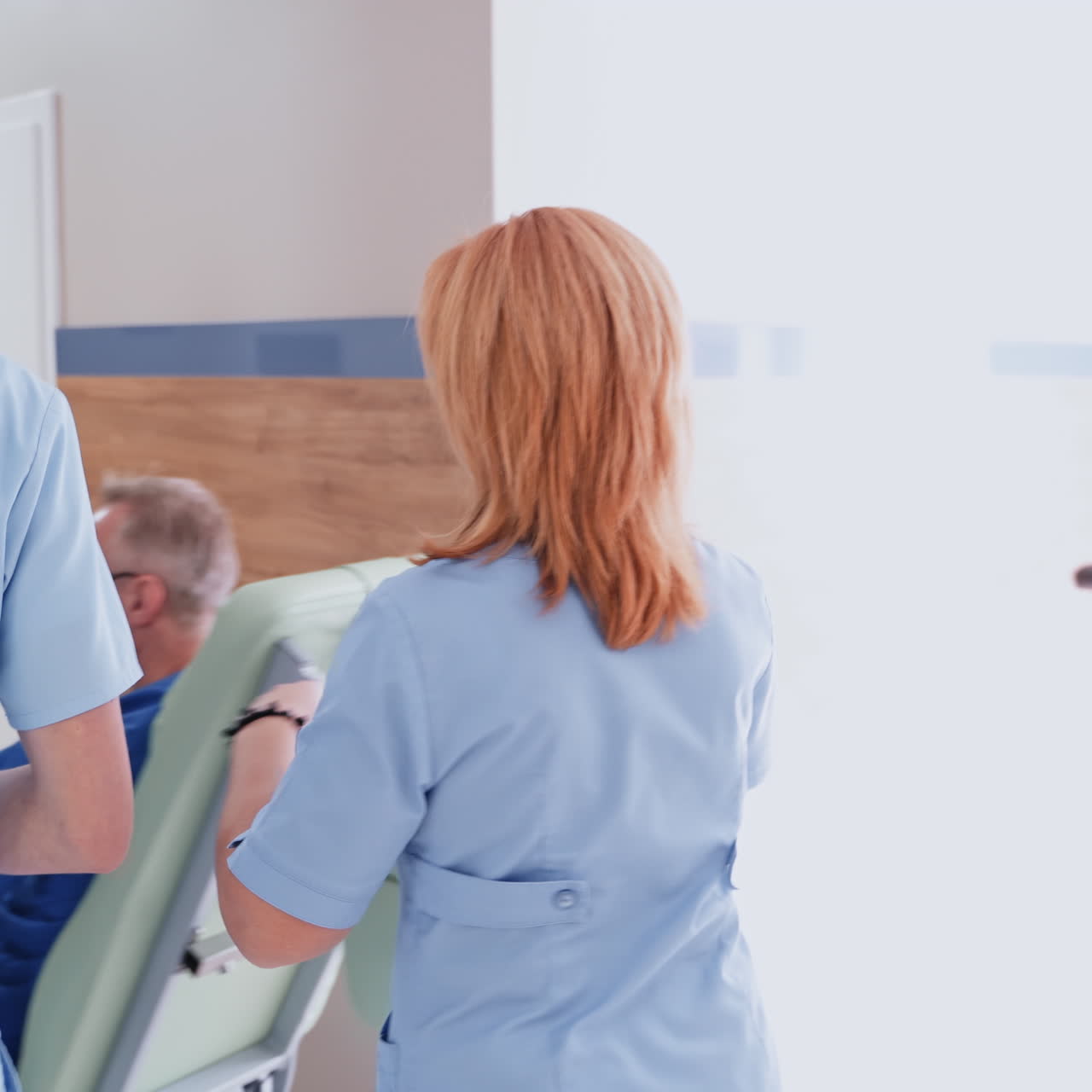Doctor and his assistant in clinic. Female nurse pushing a wheelchair with a sick patient on the hallway. Back view of medical workers in the hospital corridor.