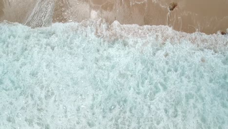 Waves-breaking-onto-beach-with-some-rocks,-rising-drone-shot