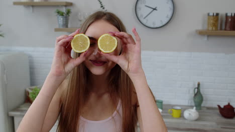 joyful young girl vegan holding fresh halves of lemon on eyes and fooling around, making funny faces