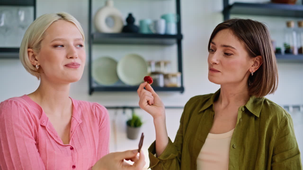 Cute lesbians eating fruits at kitchen closeup. Lgbt couple enjoying desserts