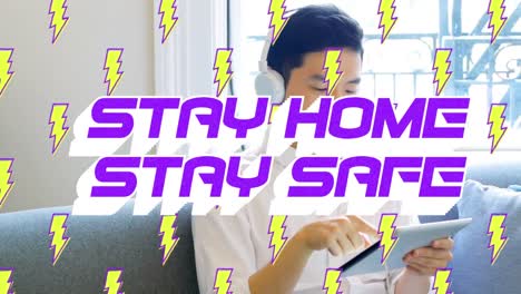 Animation of text Stay Home Stay Safe with lightnings icons floating over Asian man using a tablet