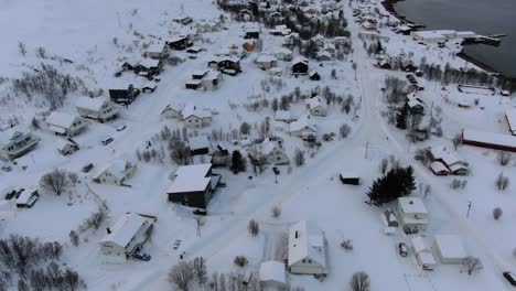 Vista-De-Drones-En-La-Zona-De-Tromso-En-Invierno-Volando-Sobre-Un-Pequeño-Pueblo-Con-Un-Paisaje-Lleno-De-Nieve-Junto-A-Un-Fiordo-En-Noruega