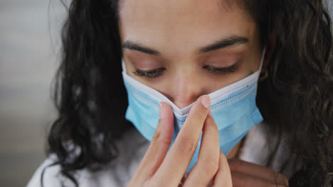 Portrait-close-up-of-mixed-race-woman-with-long-dark-hair-putting-face-mask-on-in-slow-motion