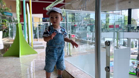 curious caucasian toddler boy stands near the glass fence in the mall. little kid looking down.