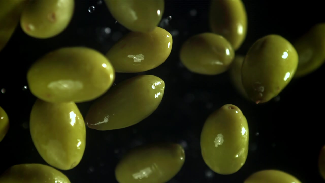 Olive verdi fresche che cadono al rallentatore con goccioline d'acqua