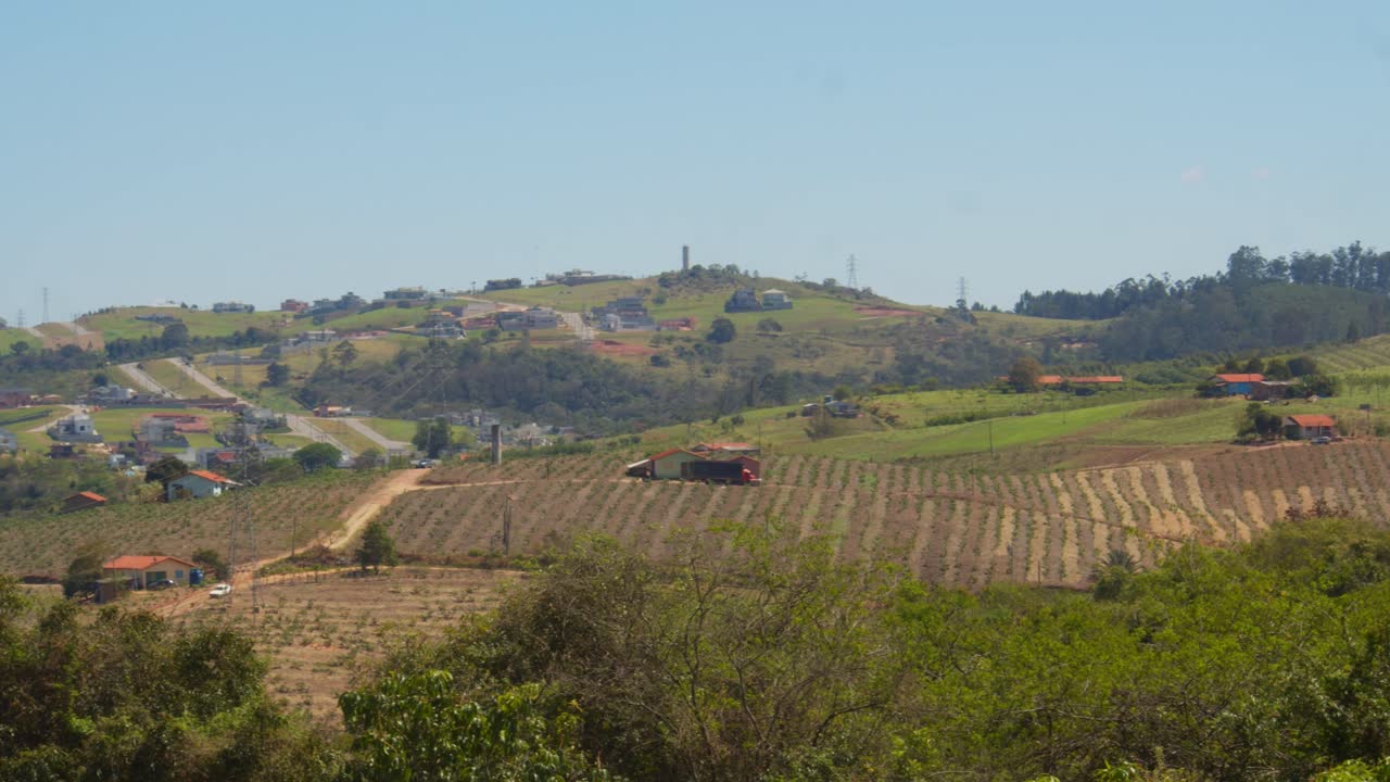 Vista lontana di piccole e semplici fattorie sulle colline del Brasile, divise da strade sterrate e sentieri che portano a piccole case contadine in mezzo ai campi coltivati, in una calma mattina di primavera.