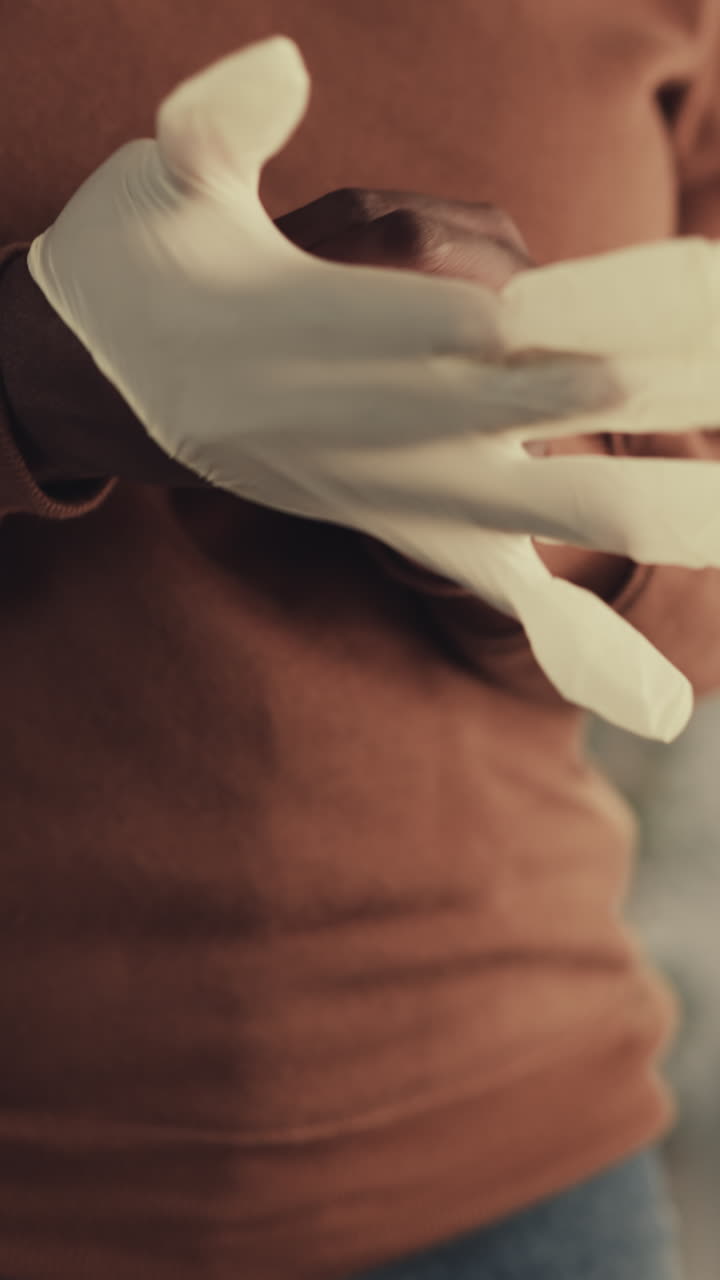 афроамериканская женщина надевает белые резиновые перчатки дома, чтобы убирать на размытом фоне. домохозяйка заботится о личной гигиене вблизи