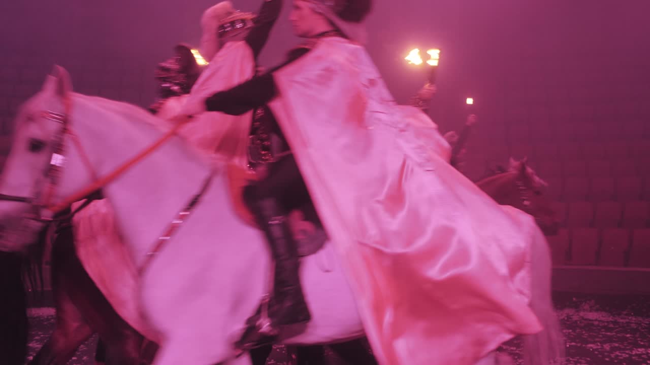 jinetes a caballo pasan por la arena del circo, con antorchas en las manos, abrigos de lluvia revoloteando, actuación