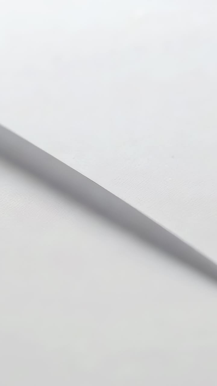 Vertical video: Panning camera revealing stacked white paper on flat tabletop, edges softening