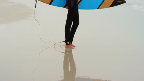 Side-view-of-active-senior-African-American-female-surfer-with-surfboard-standing-on-the-beach-4k