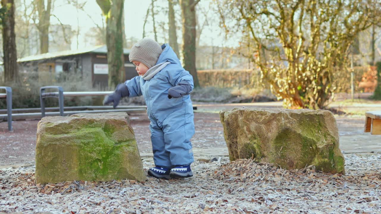 Småbarnspojke i vinteroverall leker utomhus på lekplatsen. Barn på promenad utomhus på vintern. Vinterkläder för små barn.