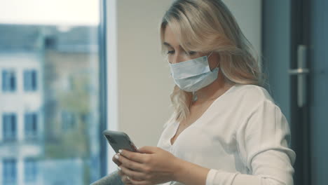 mujer de negocios con mascarilla enviando mensajes de negocios con un teléfono inteligente en la oficina
