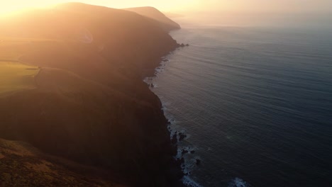 sunset view of english coast with calm sea and rural farming fields with bright sun flare setting over hills. aerial drone natural scenery environment ocean footage 4k.