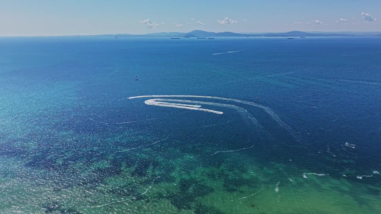 Barcos criam ondas em água azul durante um dia ensolarado na praia.