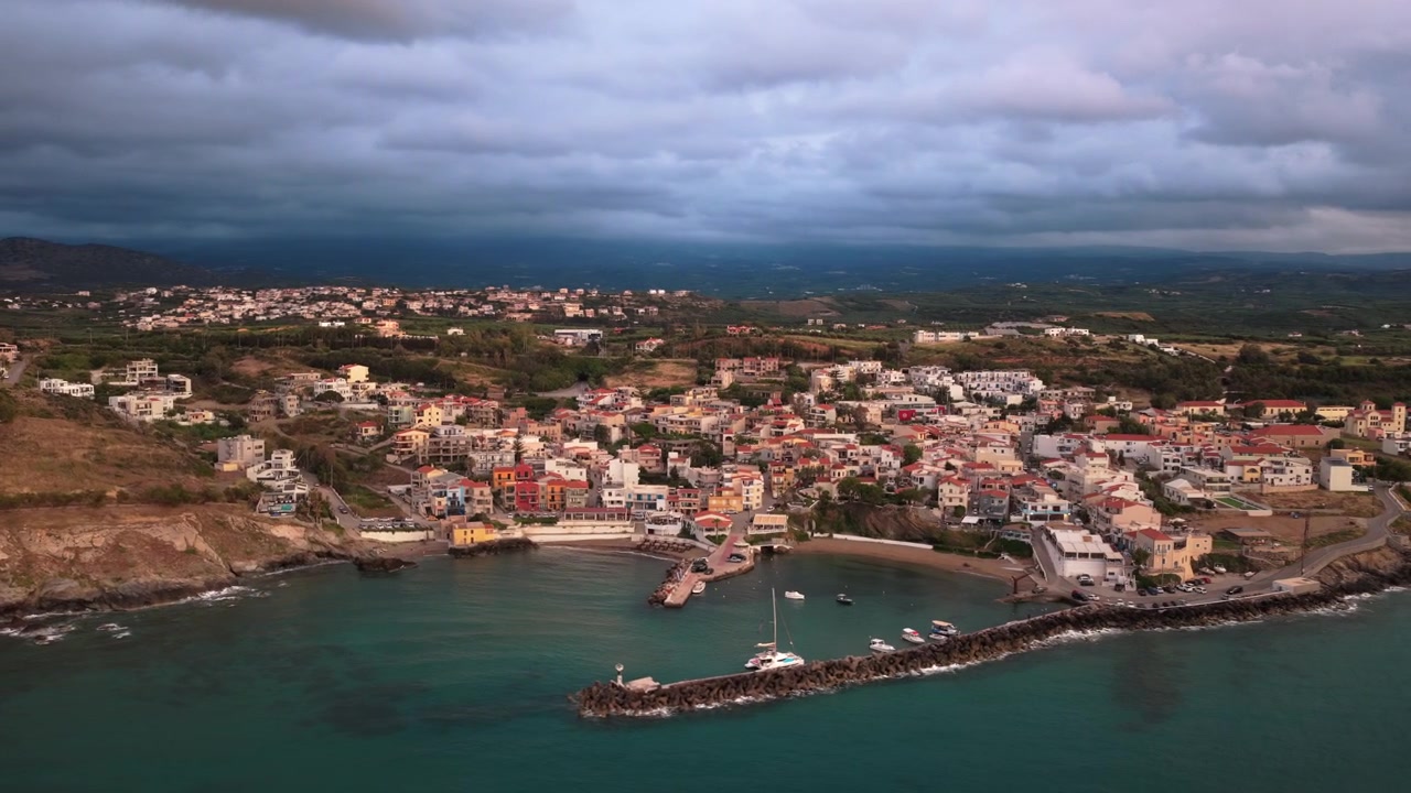 Vista aerea con drone del porto e del frangiflutti di un colorato villaggio costiero con case dai tetti rossi, Panormos, Grecia