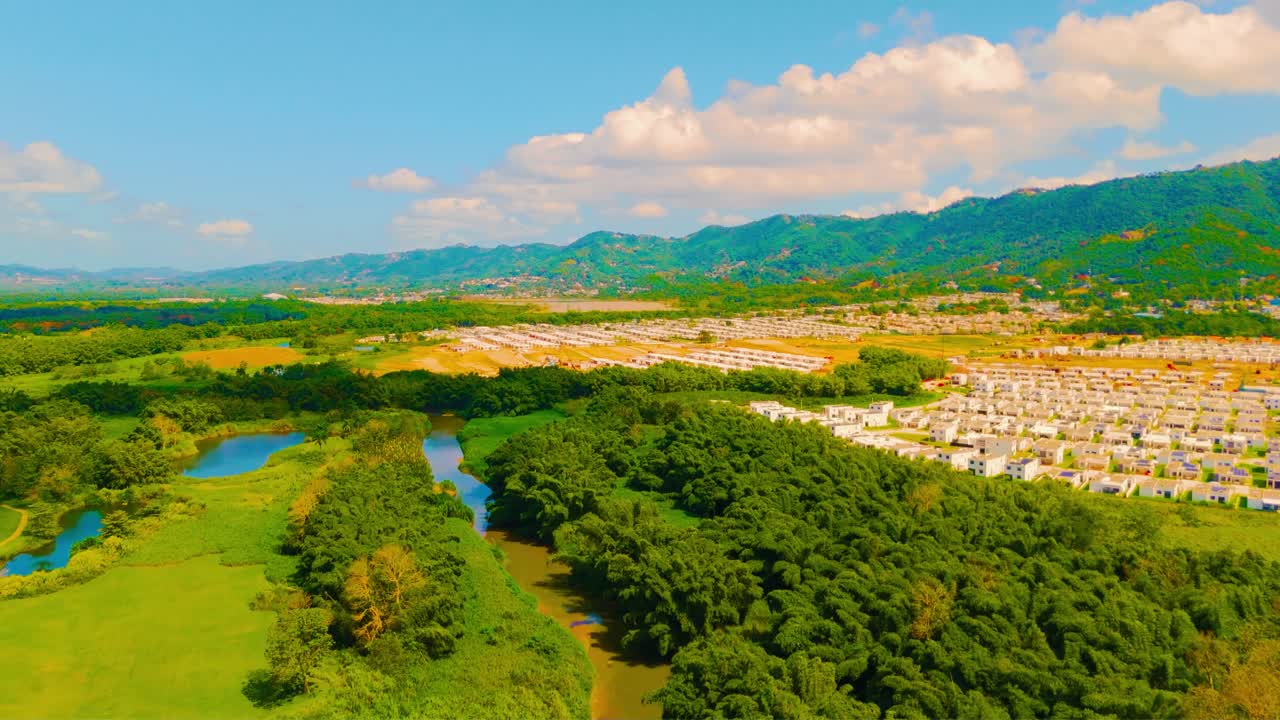 Drone footage of Gurabo River winding through lush trees beside community construction in Puerto Rico, filmed in late morning light. Perfect for real estate, environment, and infrastructure visuals