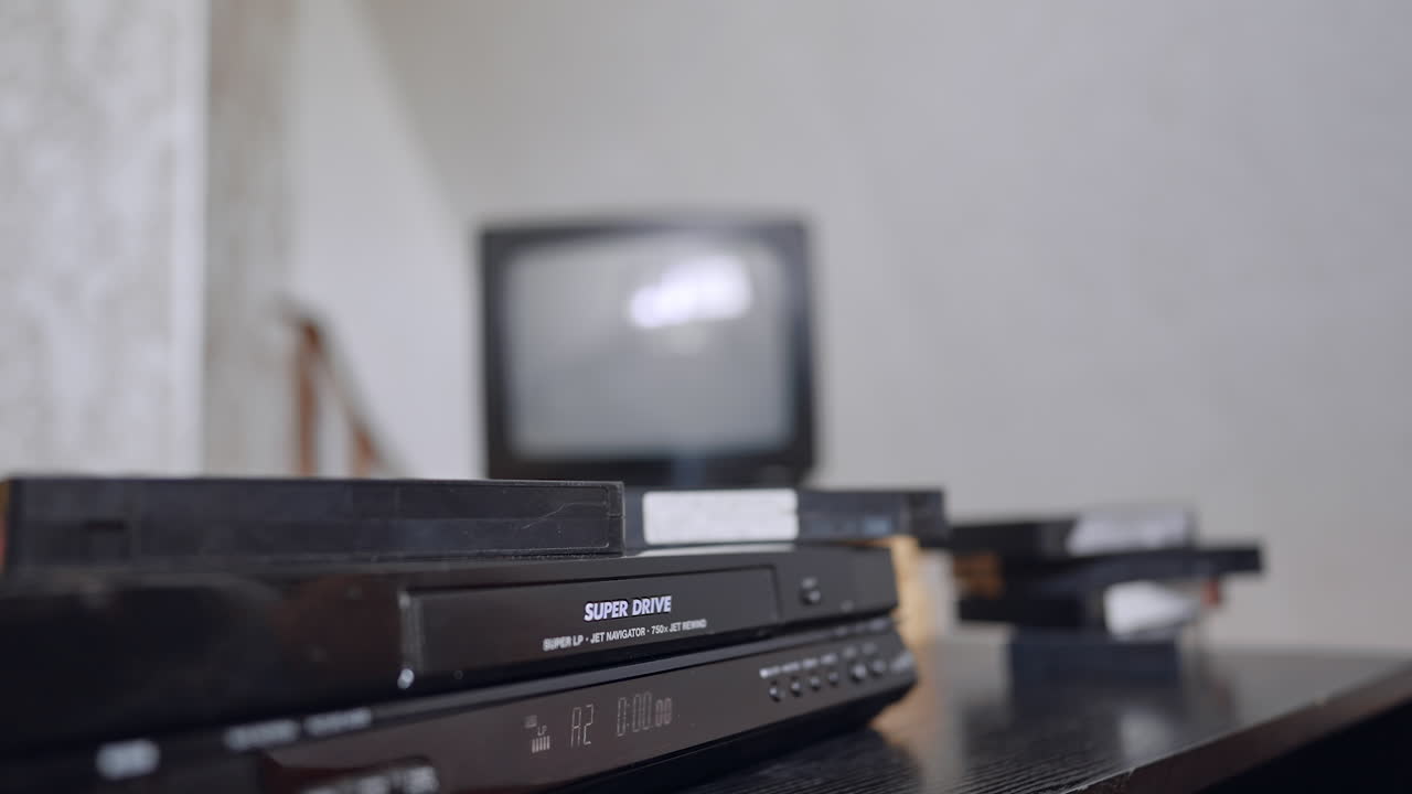 Hand loading tape into VCR slot. A hand gently places a VHS cassette into the front slot of an old video recorder