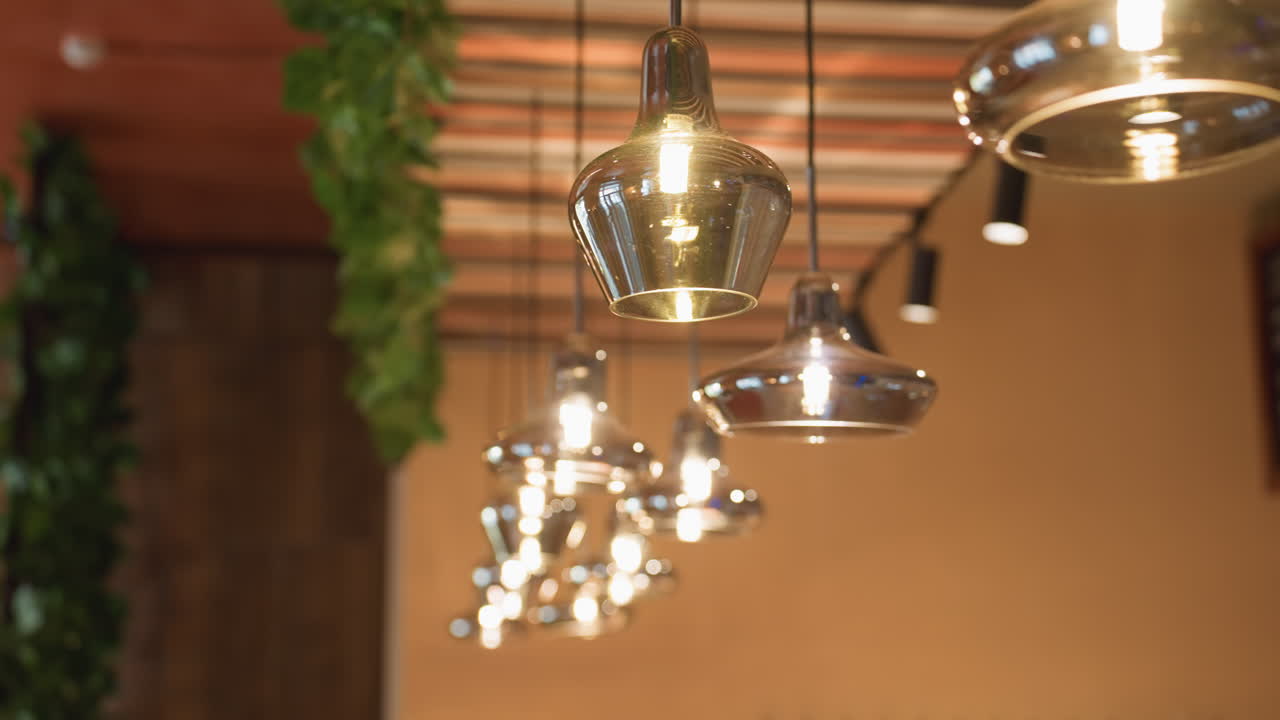 Close up of glowing glass pendant lights hanging from striped ceiling in stylish bar interior, with soft focus creating cozy and refined atmosphere accented by trailing green ivy decor