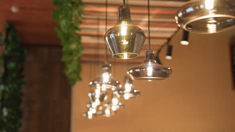 close up of glowing glass pendant lights hanging from striped ceiling in stylish bar interior, with soft focus creating cozy and refined atmosphere accented by trailing green ivy decor