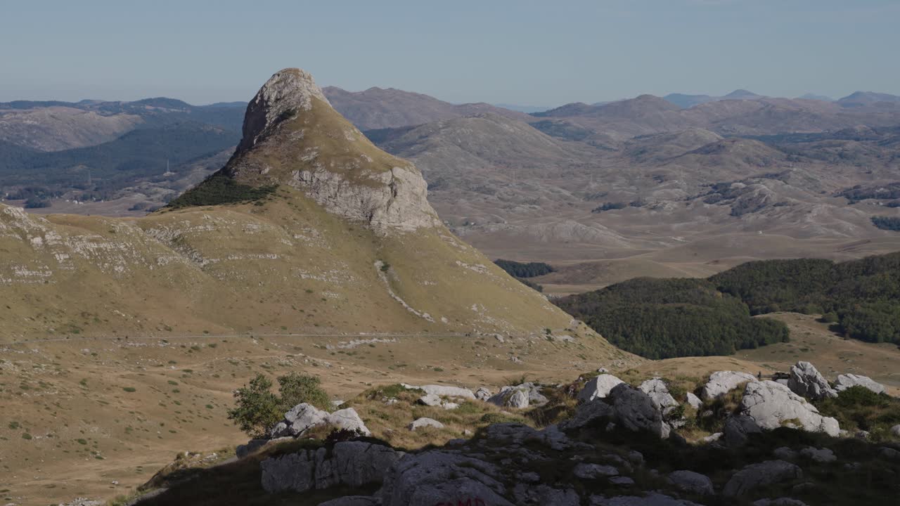 Pointed rocky peak rises sharply over dry highlands and forest patches in Durmitor National Park, Montenegro