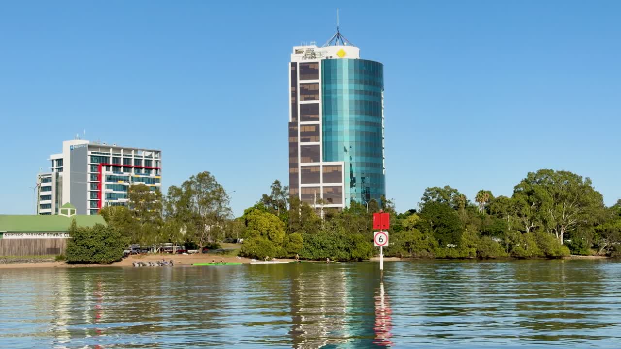 Plano general estático de edificios de cristal contemporáneos reflejados en la tranquila agua de un río bajo un cielo azul