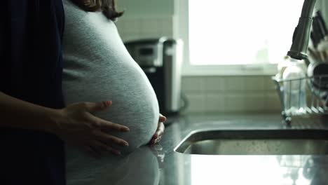 pregnant woman touching her belly in kitchen