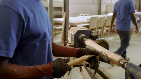 men working in shop guiding blank turning on lathe for technique practice while peer drilling plank