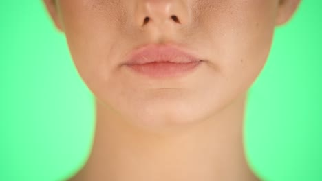 Extreme-close-up-of-a-young-pretty-woman-while-her-lips-are-shown-and-she-is-eating-a-vegan-lemon-flavored-candy-and-enjoying-the-sweetness-in-her-mouth-against-green-background-in-slow-motion