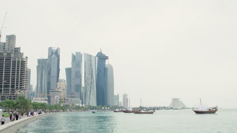 people waling on corniche with dhow boats and skyline of doha